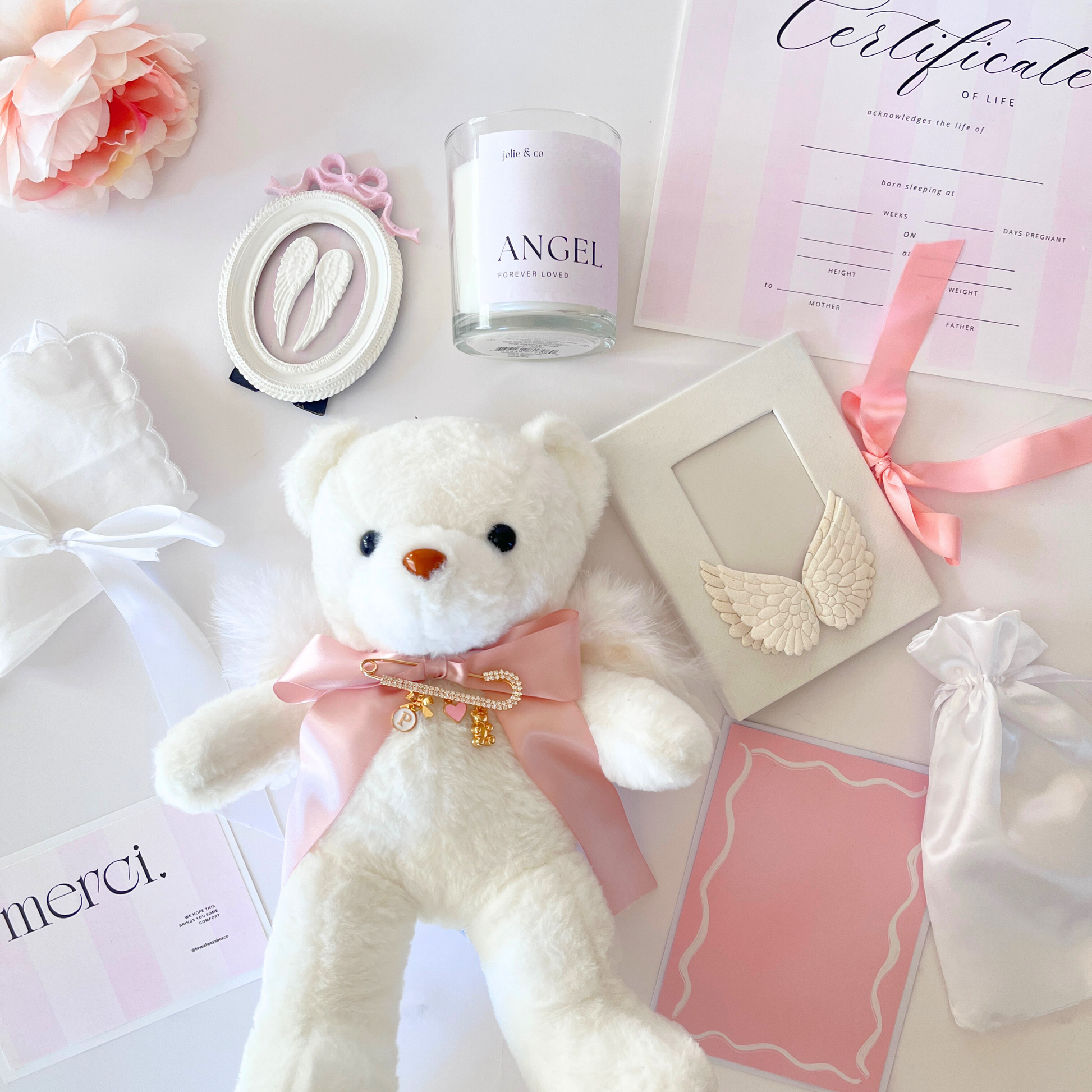White teddy bear with pink bow, angel candle, and certificate on a white background